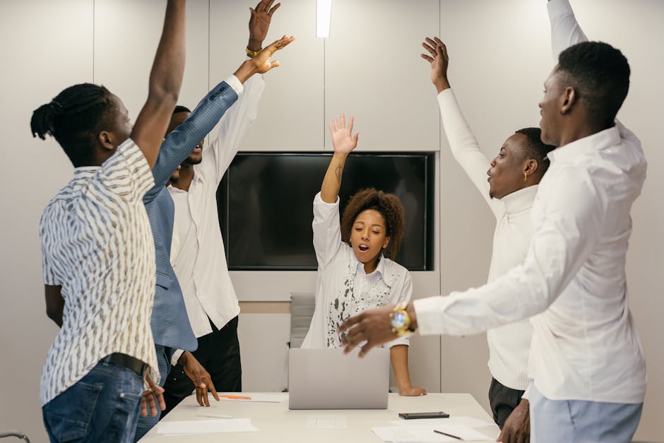 Group of diverse professionals raising hands during a collaborative team meeting in a modern office.